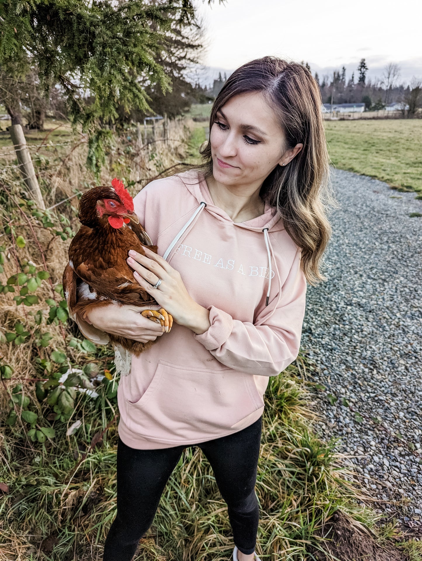 women holding a chicken while wearing a free as a bird hoodie